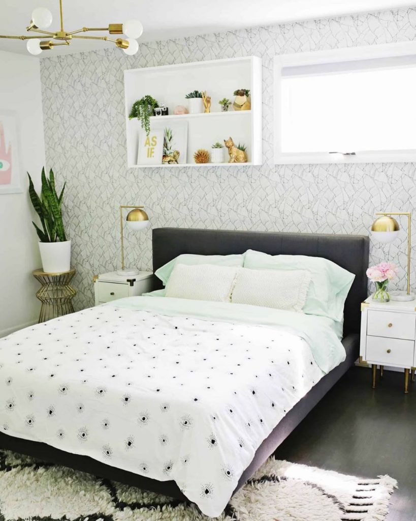 instagram de decoração cama com cabeceira preta, abajours dourados, prateleiras acima da cama brancas, lençol branco, planta no quarto