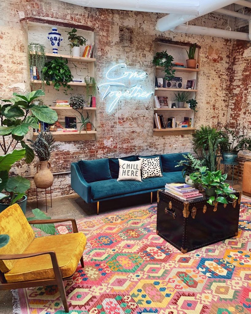 instagram de decoração sala com sofá azul e poltrona amarela, tapete colorido, flores verdes e prateleiras 