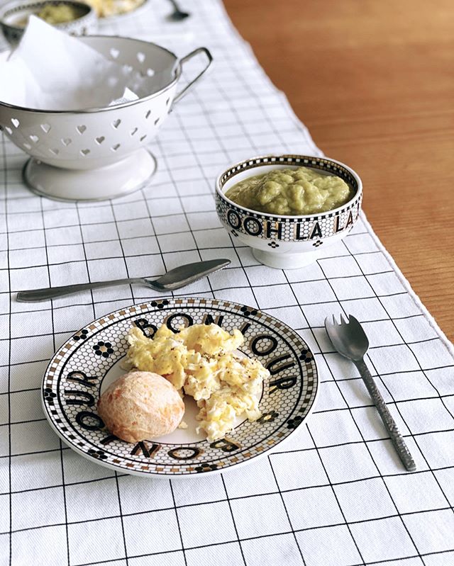rotina diária - café da manhã - toalha quadriculada sobre a mesa com prato e talheres com pão de queijo e ovos em cima e um escorredor de macarrão com guardanapo acima, para enfeite